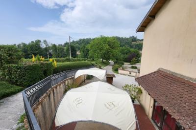 Grande maison en pierre entourée de verdure, avec une cour ensoleillée et des arbres en arrière-plan.