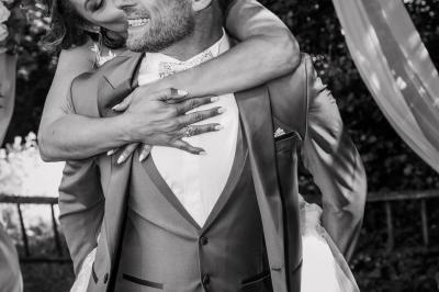 Grande maison en pierre entourée de verdure, avec une cour ensoleillée et des arbres en arrière-plan.