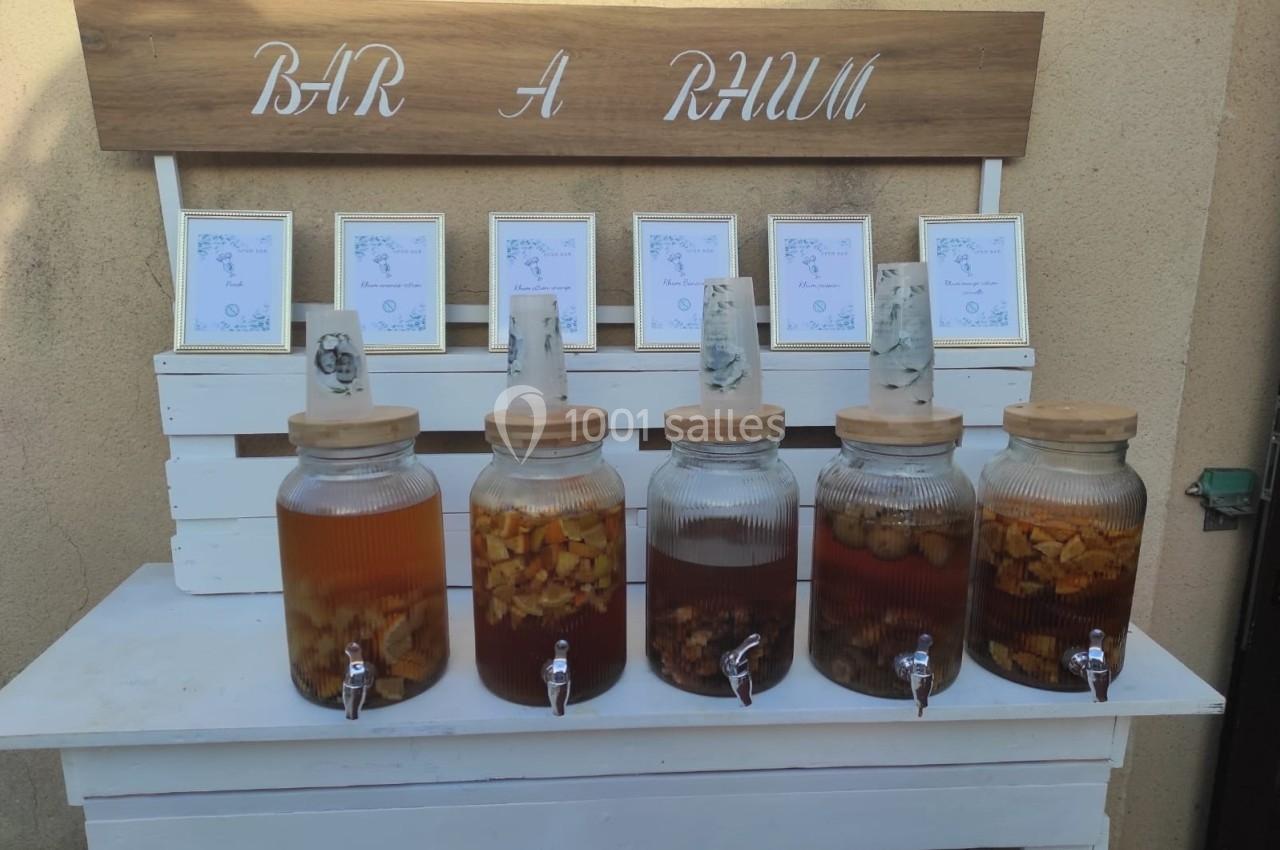 Bar à rhum avec cinq bocaux en verre contenant des préparations infusées, disposés sur un meuble en bois blanc.