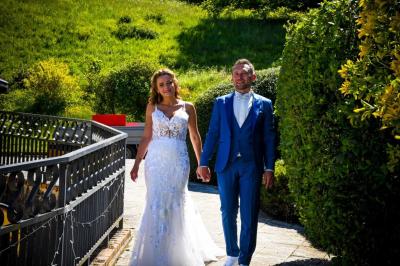 Grande maison en pierre entourée de verdure, avec une cour ensoleillée et des arbres en arrière-plan.