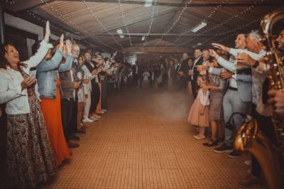 Grande maison en pierre entourée de verdure, avec une cour ensoleillée et des arbres en arrière-plan.