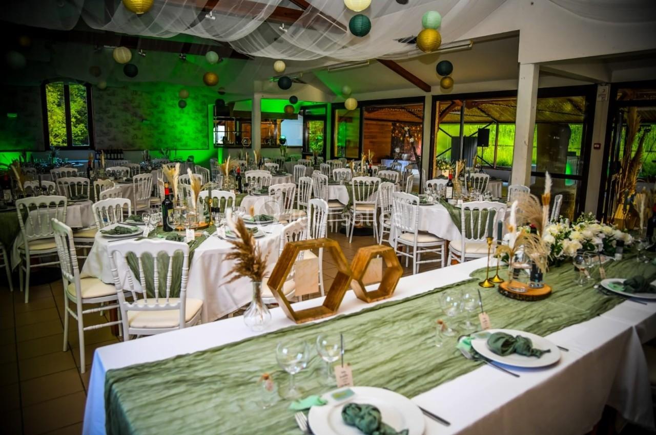 Salle de réception décorée pour un événement, avec tables dressées, nappes vertes et blanches, et suspensions colorées.