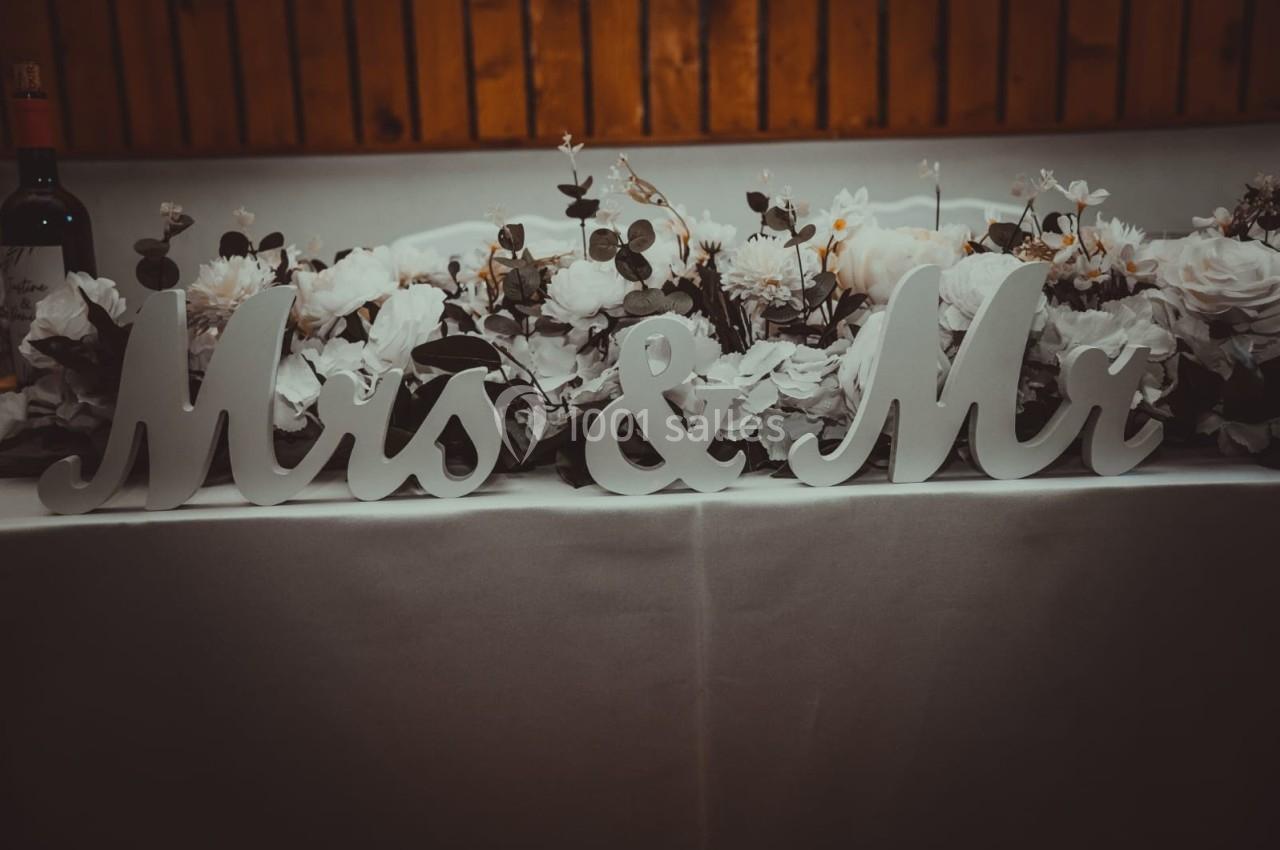 Décoration de table de mariage avec des lettres ’Mrs & Mr’ entourées de fleurs blanches et feuillages.