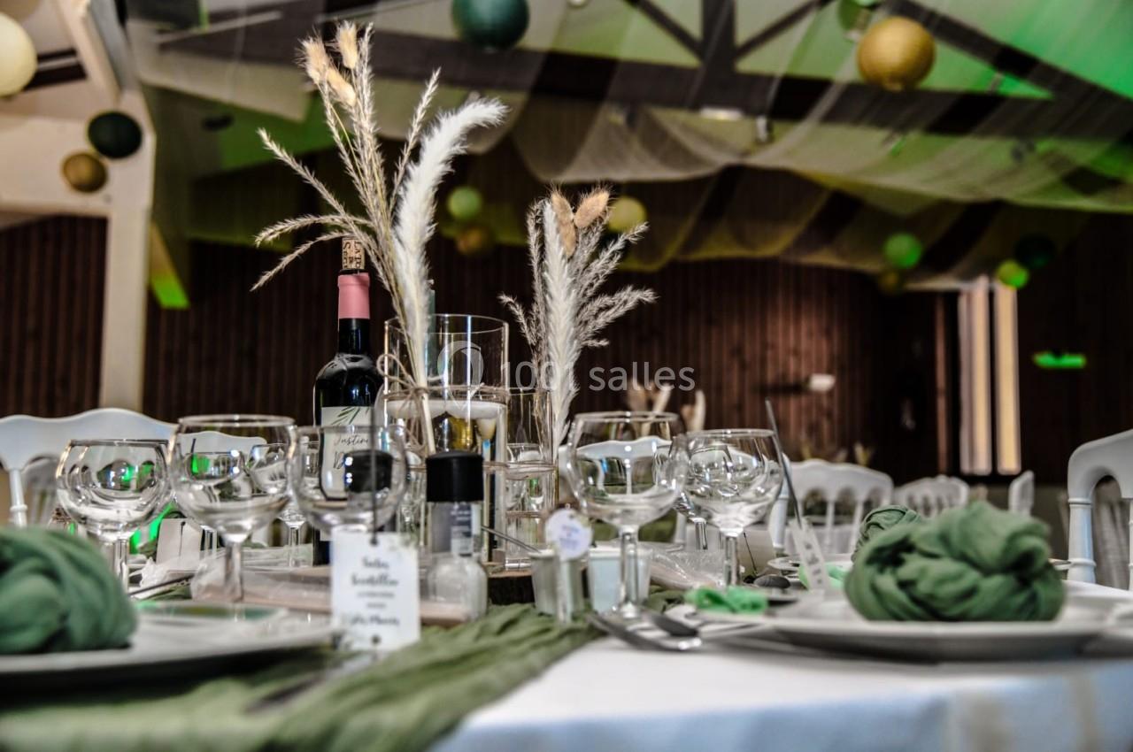 Table dressée avec des verres, une bouteille de vin, des décorations végétales et des serviettes vertes dans une salle…
