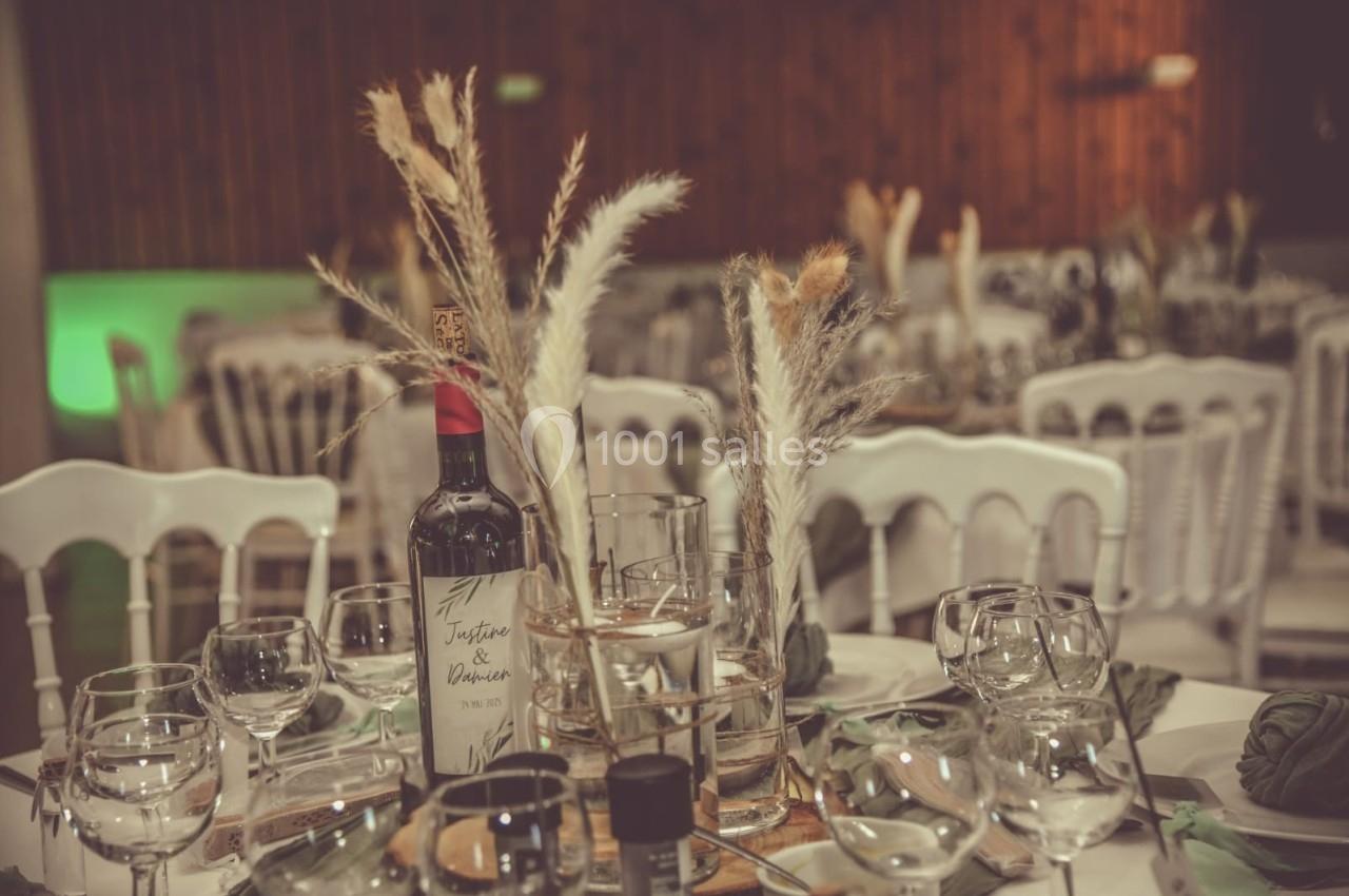 Table décorée pour un événement avec bouteille de vin, verres, pampas et chaises blanches en arrière-plan.