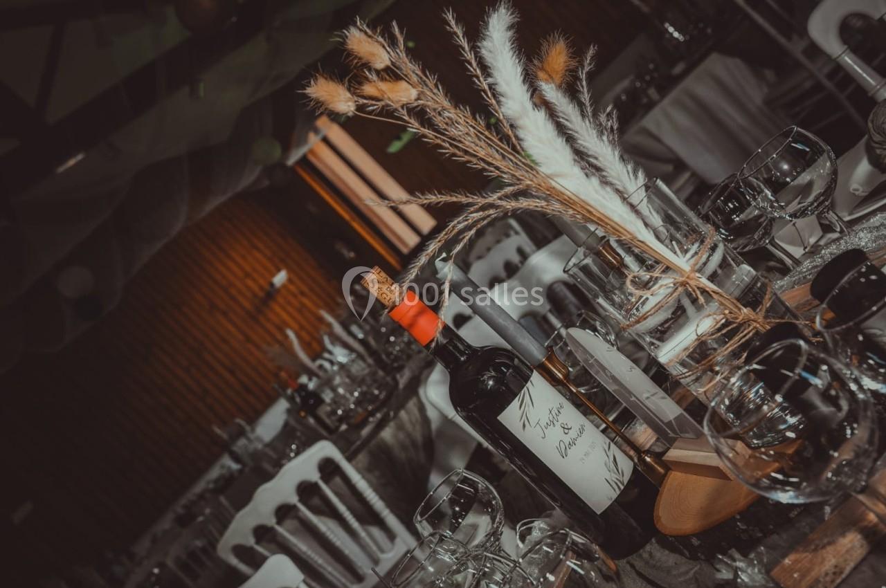 Bouteille de vin rouge et décoration florale sur une table dressée avec des verres dans une salle de réception.