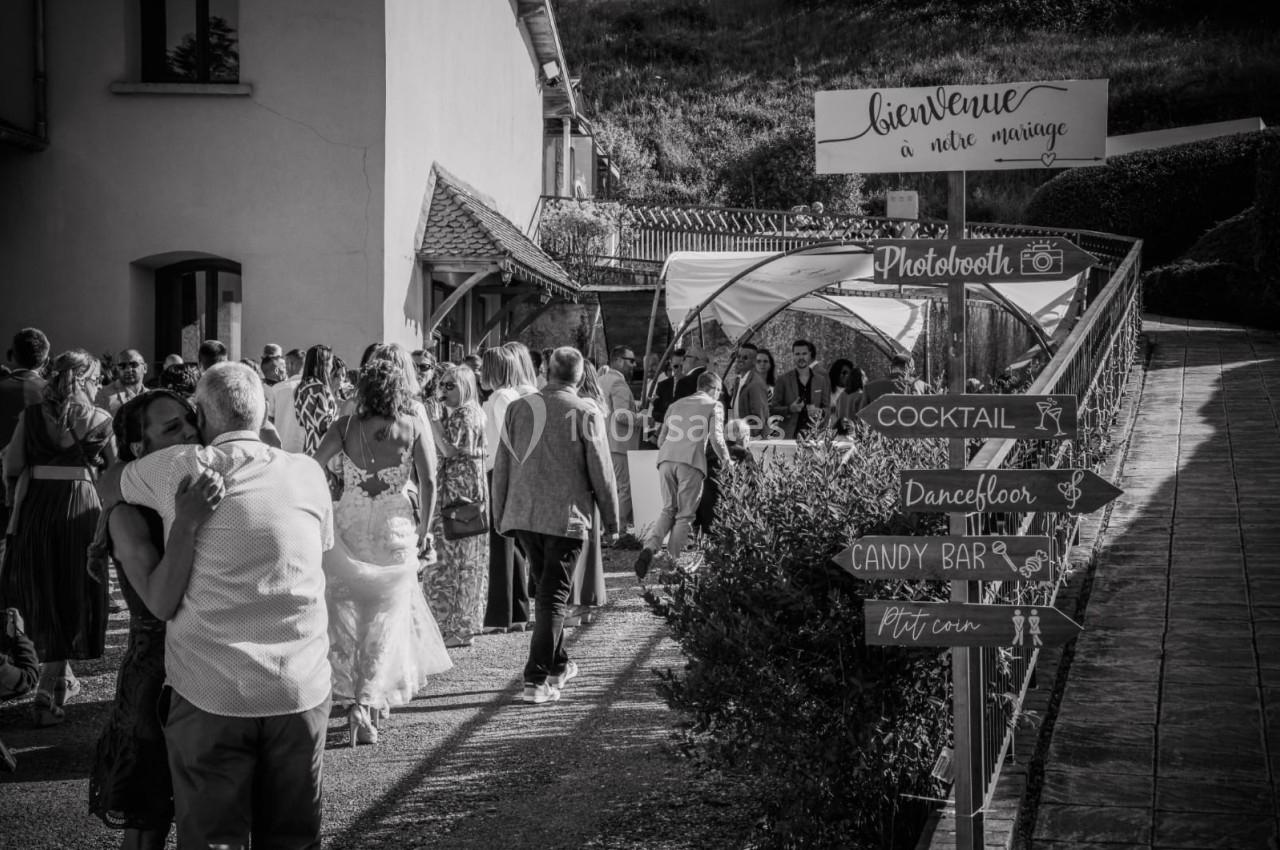 Groupe de personnes rassemblées lors d'un mariage en extérieur, avec des panneaux indiquant différentes activités.