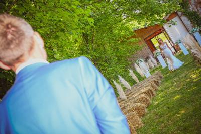 Grande maison en pierre entourée de verdure, avec une cour ensoleillée et des arbres en arrière-plan.