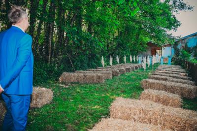 Grande maison en pierre entourée de verdure, avec une cour ensoleillée et des arbres en arrière-plan.