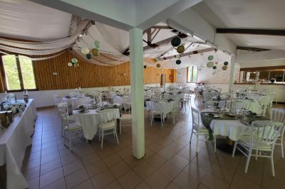 Grande maison en pierre entourée de verdure, avec une cour ensoleillée et des arbres en arrière-plan.