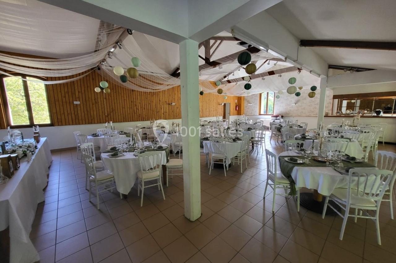 Salle de réception décorée avec des tables rondes et rectangulaires, nappes blanches et suspensions colorées.