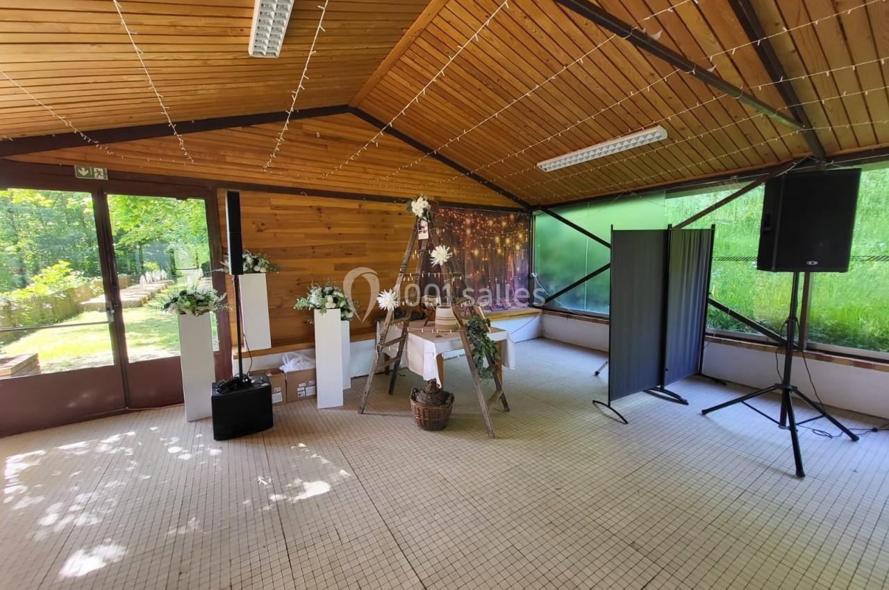 Salle en bois décorée pour un événement, avec arche florale, guirlandes lumineuses et grandes baies vitrées donnant sur un…