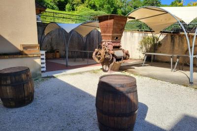 Grande maison en pierre entourée de verdure, avec une cour ensoleillée et des arbres en arrière-plan.