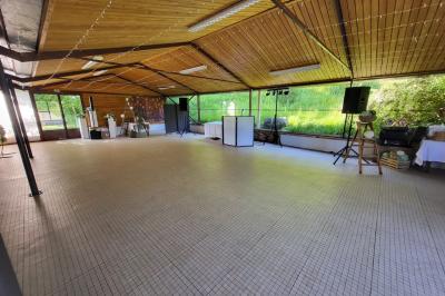 Grande maison en pierre entourée de verdure, avec une cour ensoleillée et des arbres en arrière-plan.