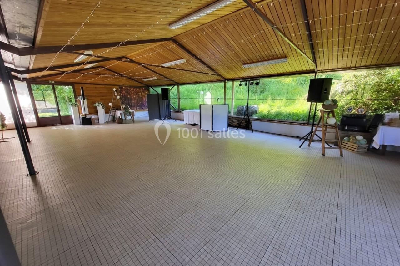 Salle lumineuse avec plafond en bois, carrelage clair, tables décorées et équipements audio près de grandes baies vitrées.