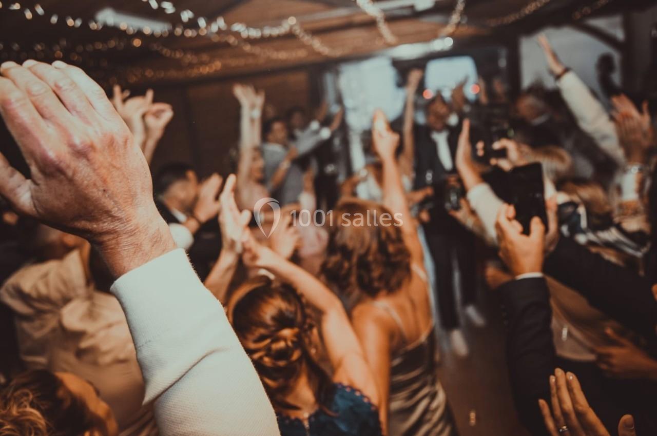Groupe de personnes dansant et levant les bras lors d'une fête dans une salle décorée de guirlandes lumineuses.
