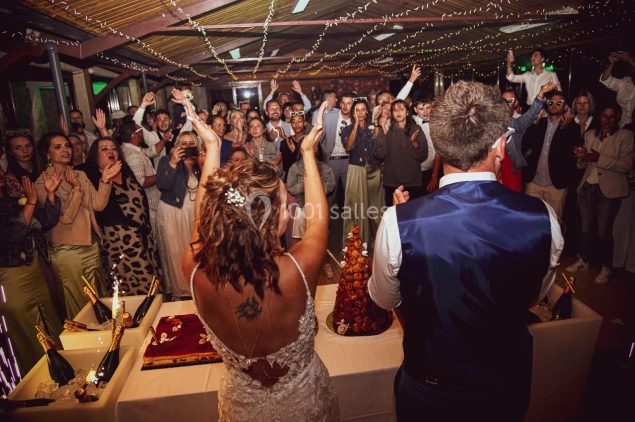 Un couple de mariés de dos face à des invités applaudissant sous des guirlandes lumineuses lors d'une réception.