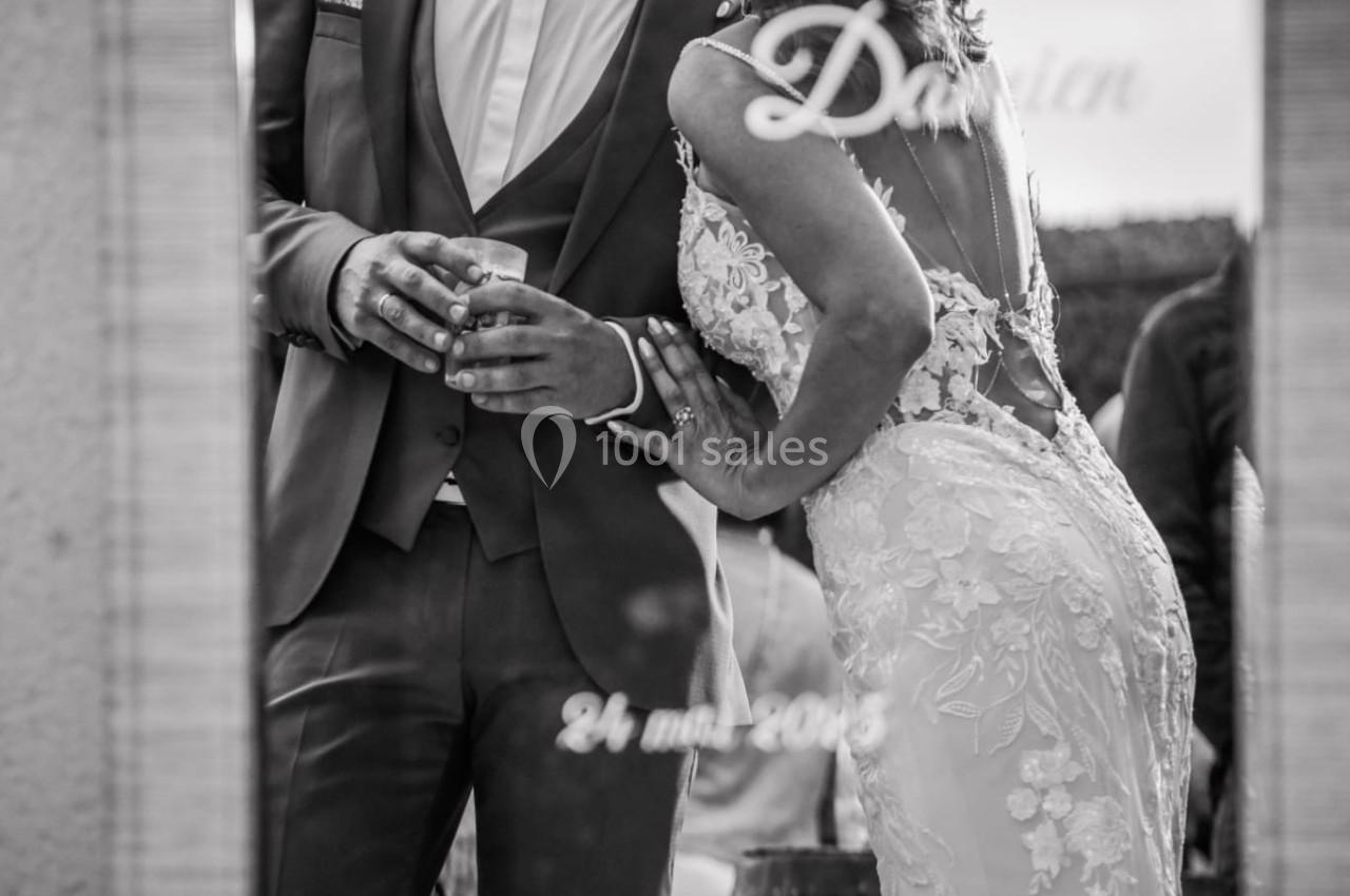 Un couple en tenue de mariage s'embrasse devant un miroir gravé avec leurs prénoms et la date de leur union.