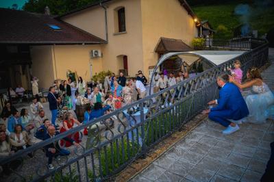 Grande maison en pierre entourée de verdure, avec une cour ensoleillée et des arbres en arrière-plan.