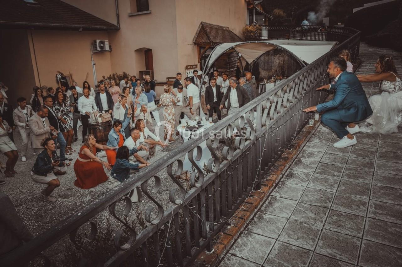 Des invités assistent à une fête en plein air, certains accroupis, d'autres debout, près d'une balustrade métallique.