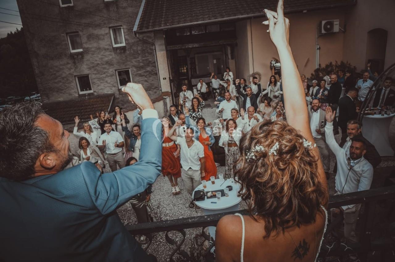 Un couple salue une foule joyeuse rassemblée dans une cour lors d'une célébration en plein air.