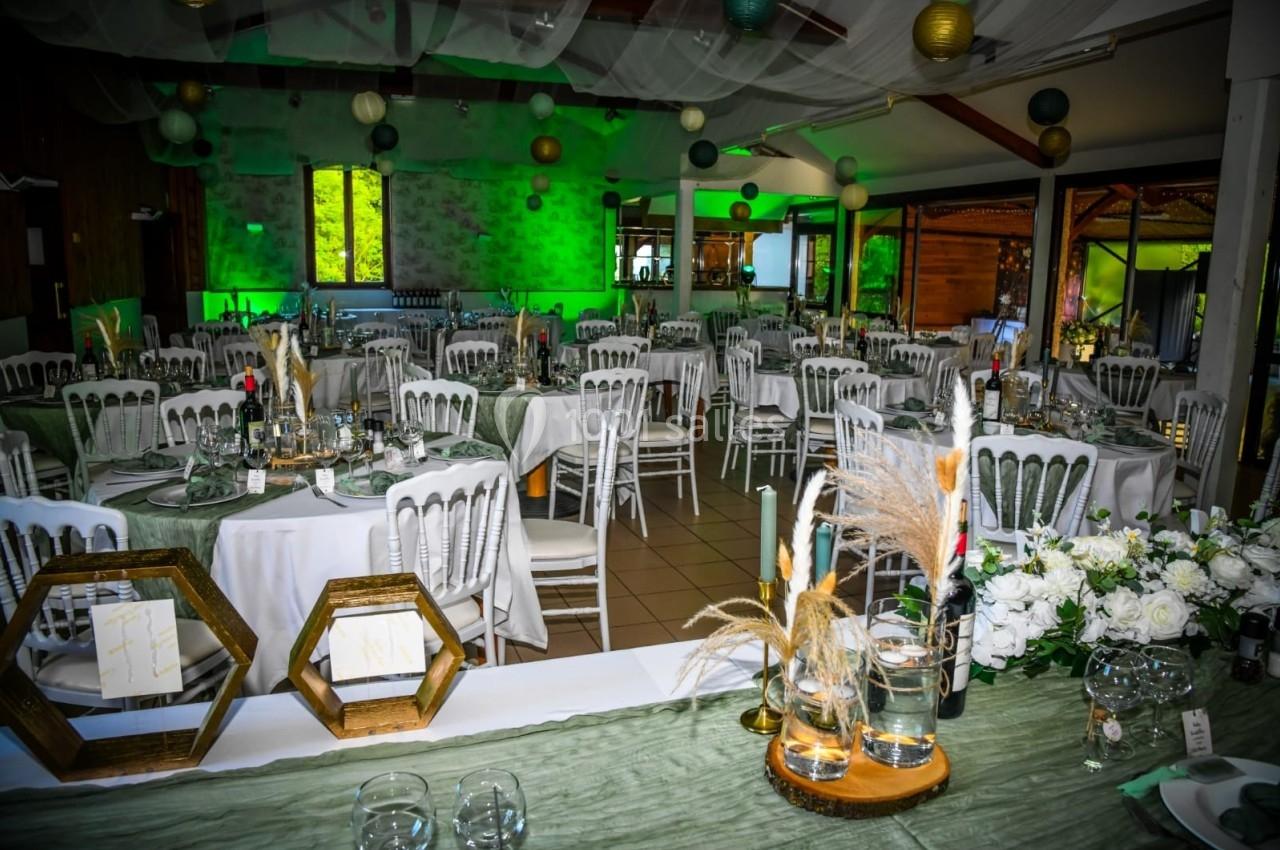 Salle décorée pour un événement avec tables dressées, chaises blanches, éclairage vert et éléments décoratifs élégants.