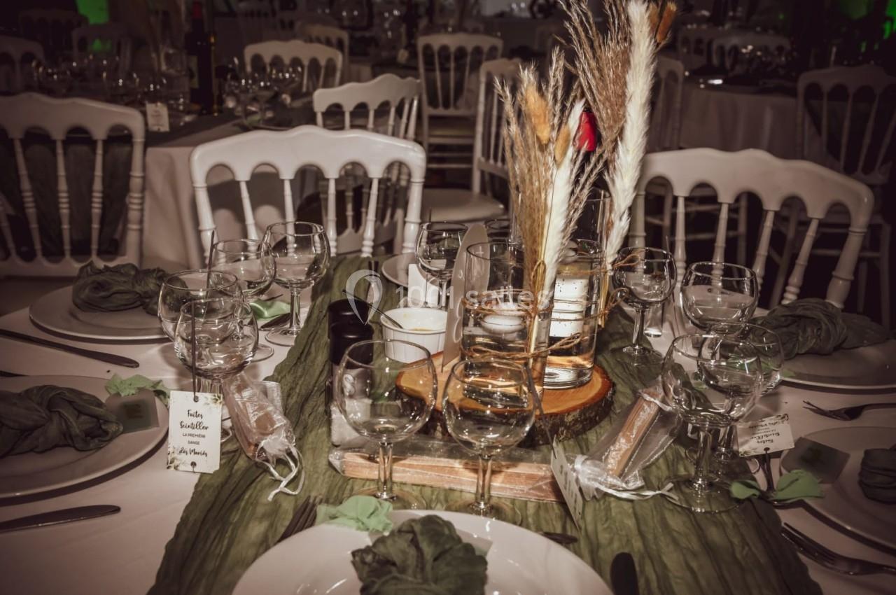 Table dressée avec nappes vertes, verres, couverts, serviettes pliées et décoration centrale avec fleurs séchées.
