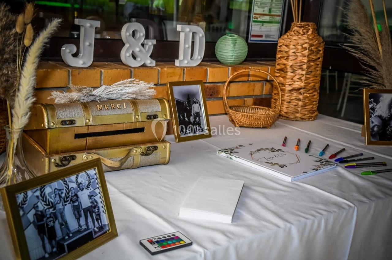 Table décorée avec des cadres photo, un coffre doré, des paniers en osier et un livre d'or entouré de stylos colorés.