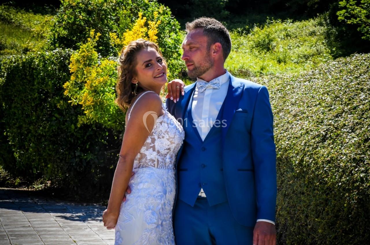 Un couple en tenue de mariage pose dans un jardin verdoyant sous une lumière ensoleillée.
