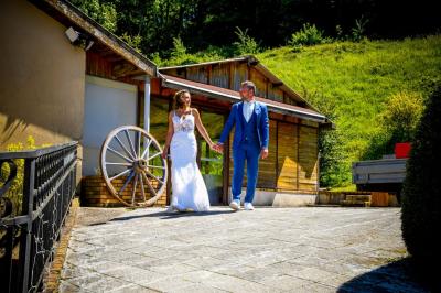 Grande maison en pierre entourée de verdure, avec une cour ensoleillée et des arbres en arrière-plan.