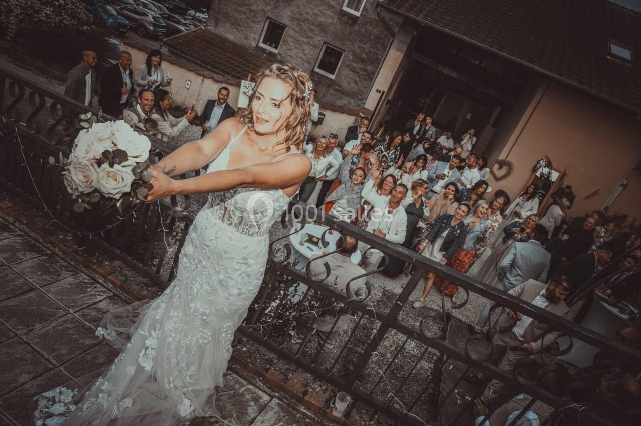 Une mariée lance son bouquet depuis un balcon devant un groupe d'invités rassemblés en contrebas.