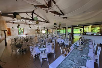 Grande maison en pierre entourée de verdure, avec une cour ensoleillée et des arbres en arrière-plan.