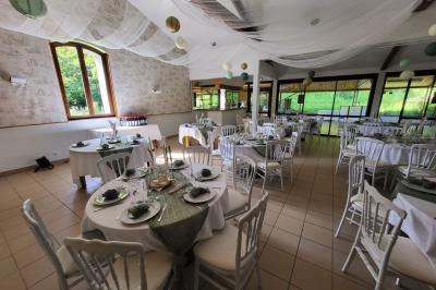 Grande maison en pierre entourée de verdure, avec une cour ensoleillée et des arbres en arrière-plan.