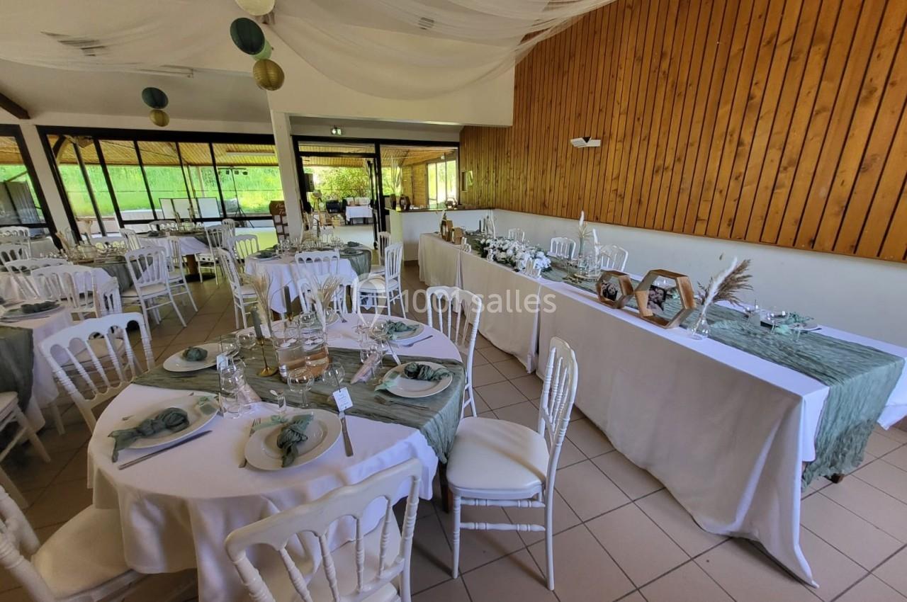 Salle de réception décorée avec des tables rondes dressées, nappes blanches et détails verts, ambiance naturelle et élégante.