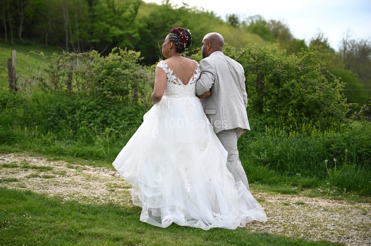 Un couple en tenue de mariage marche sur un chemin de campagne bordé de verdure.