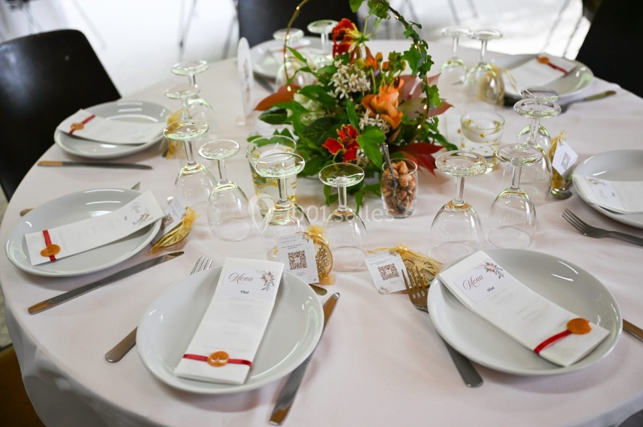 Table dressée avec une nappe blanche, des assiettes, des verres, des menus et une décoration florale au centre.