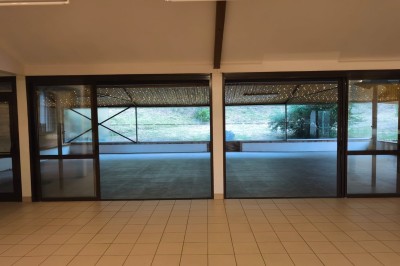 Grande maison en pierre entourée de verdure, avec une cour ensoleillée et des arbres en arrière-plan.