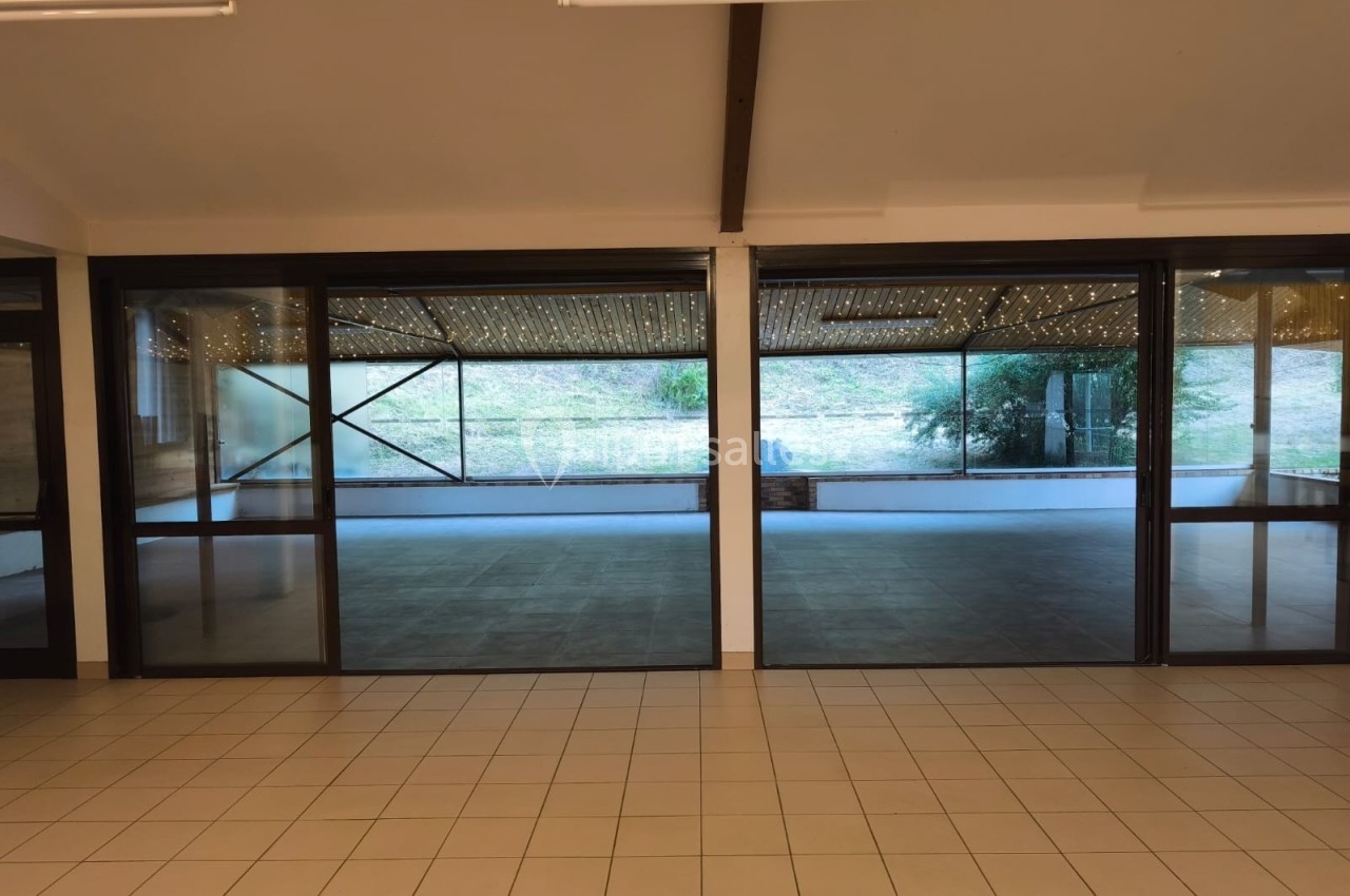 Grande baie vitrée donnant sur une terrasse couverte et un espace extérieur avec pelouse et végétation.