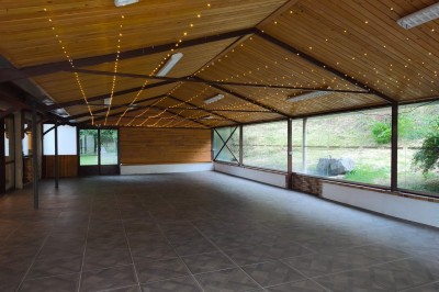 Grande maison en pierre entourée de verdure, avec une cour ensoleillée et des arbres en arrière-plan.