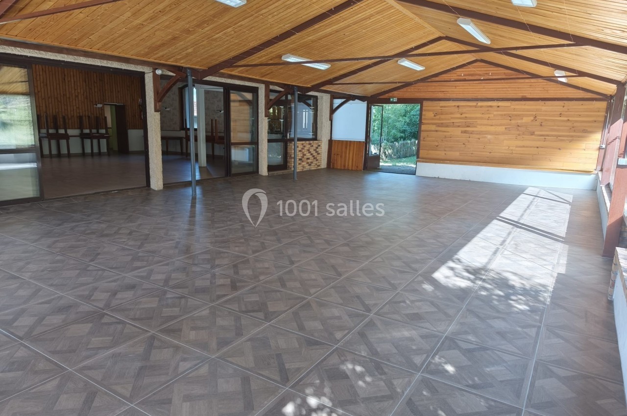 Salle spacieuse avec plafond en bois, carrelage au sol et grandes fenêtres laissant entrer la lumière naturelle.