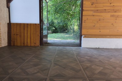 Grande maison en pierre entourée de verdure, avec une cour ensoleillée et des arbres en arrière-plan.