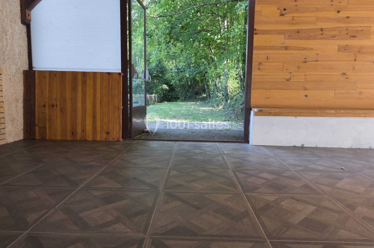 Vue d'une pièce au sol carrelé avec une porte ouverte donnant sur un jardin verdoyant.