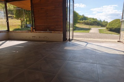 Grande maison en pierre entourée de verdure, avec une cour ensoleillée et des arbres en arrière-plan.