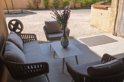 Grande maison en pierre entourée de verdure, avec une cour ensoleillée et des arbres en arrière-plan.