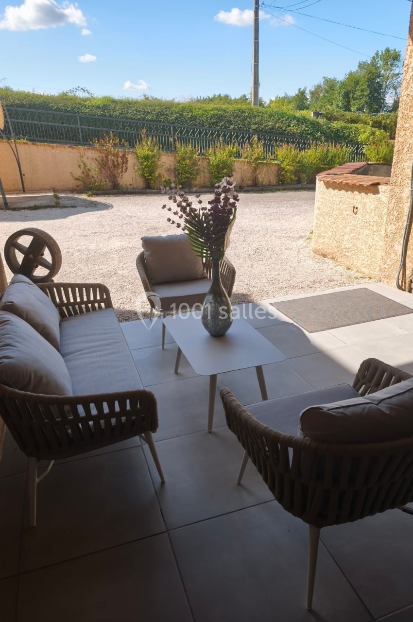 Salon de jardin avec canapé, fauteuils et table basse, installé sur une terrasse carrelée, vue sur une cour extérieure.