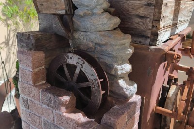 Grande maison en pierre entourée de verdure, avec une cour ensoleillée et des arbres en arrière-plan.