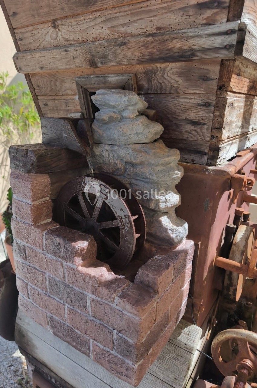 Petite roue à eau en métal intégrée à une structure en bois et briques, décorative dans un espace extérieur.
