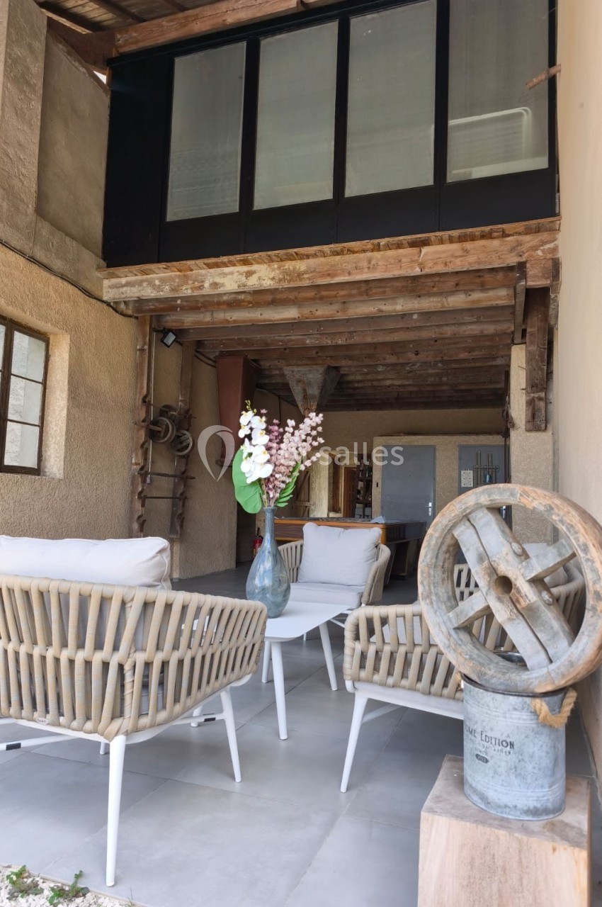 Espace extérieur couvert avec fauteuils en rotin, table basse, vase fleuri et éléments décoratifs rustiques.