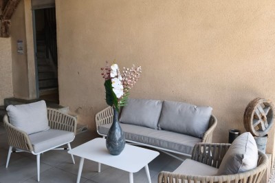 Grande maison en pierre entourée de verdure, avec une cour ensoleillée et des arbres en arrière-plan.