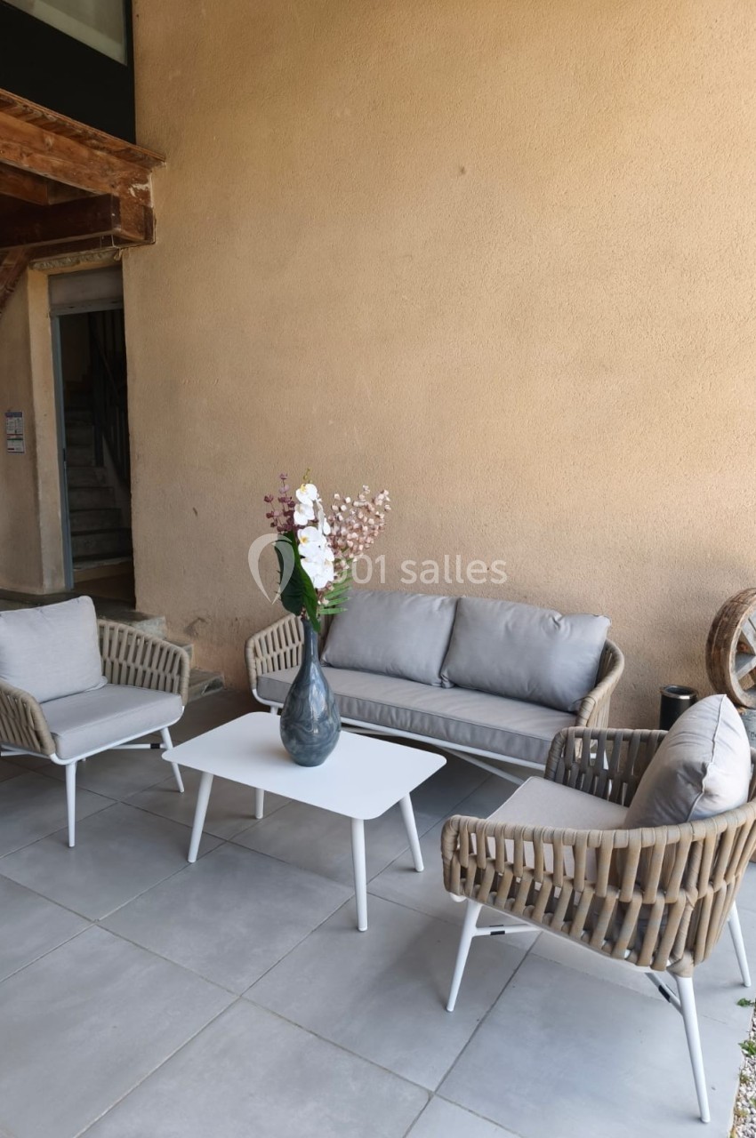 Salon de jardin avec canapé, fauteuils en rotin et table basse blanche, disposé sur une terrasse en carrelage clair.